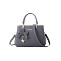 Bolso de mano Ibravacr gris de piel sintética con lazo frontal, dije de flor y herrajes dorados con correa ajustable.
