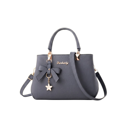 Bolso de mano Ibravacr gris de piel sintética con lazo frontal, dije de flor y herrajes dorados con correa ajustable.