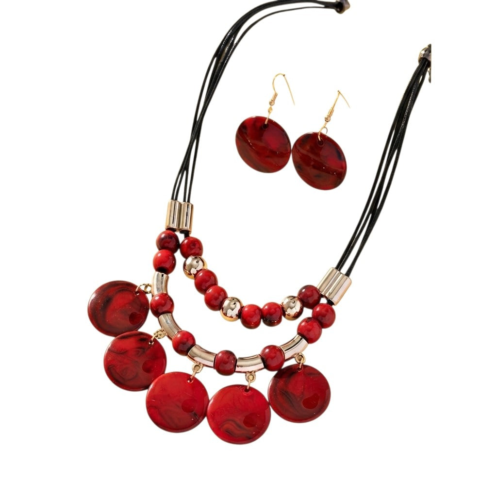 Conjunto de collar y aretes Ibravacr con cuentas rojas marmoladas, cordones negros y detalles en tono dorado.