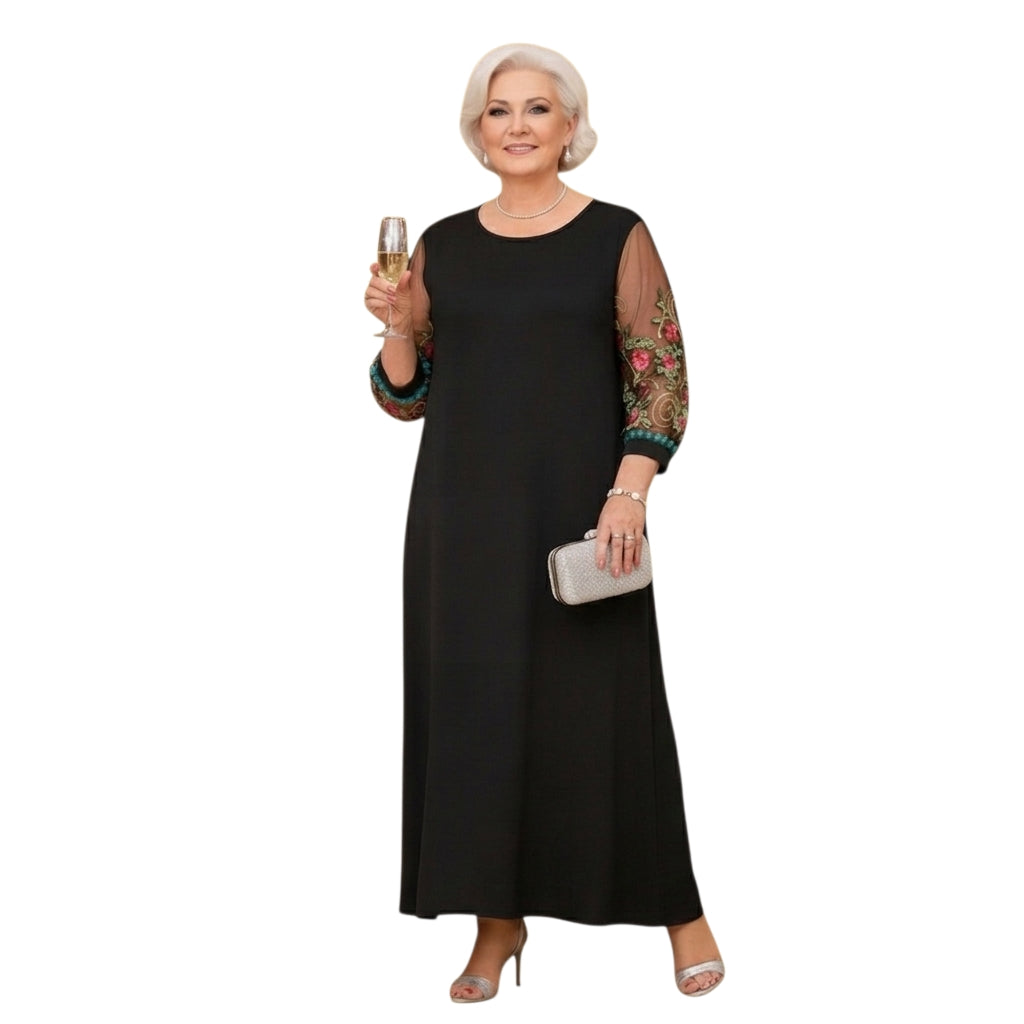Mujer madura con vestido largo negro Ibravacr de corte fluido y mangas transparentes con bordados florales coloridos.